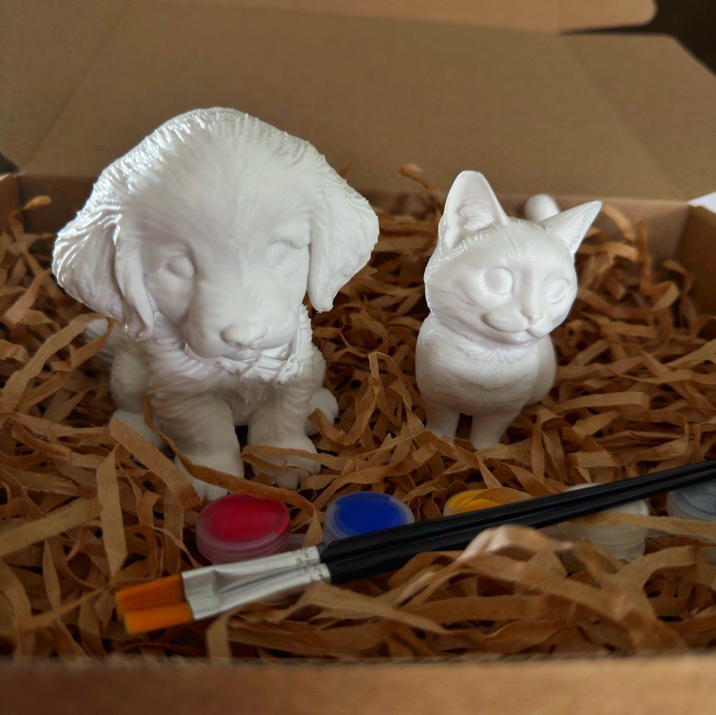 Figuras blancas de un perro y un gato con pinturas y pinceles dentro de Petbox
